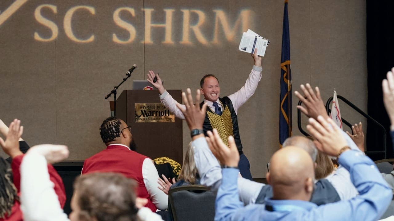 Kevin on stage at a state SHRM conference as the audience raises their hands