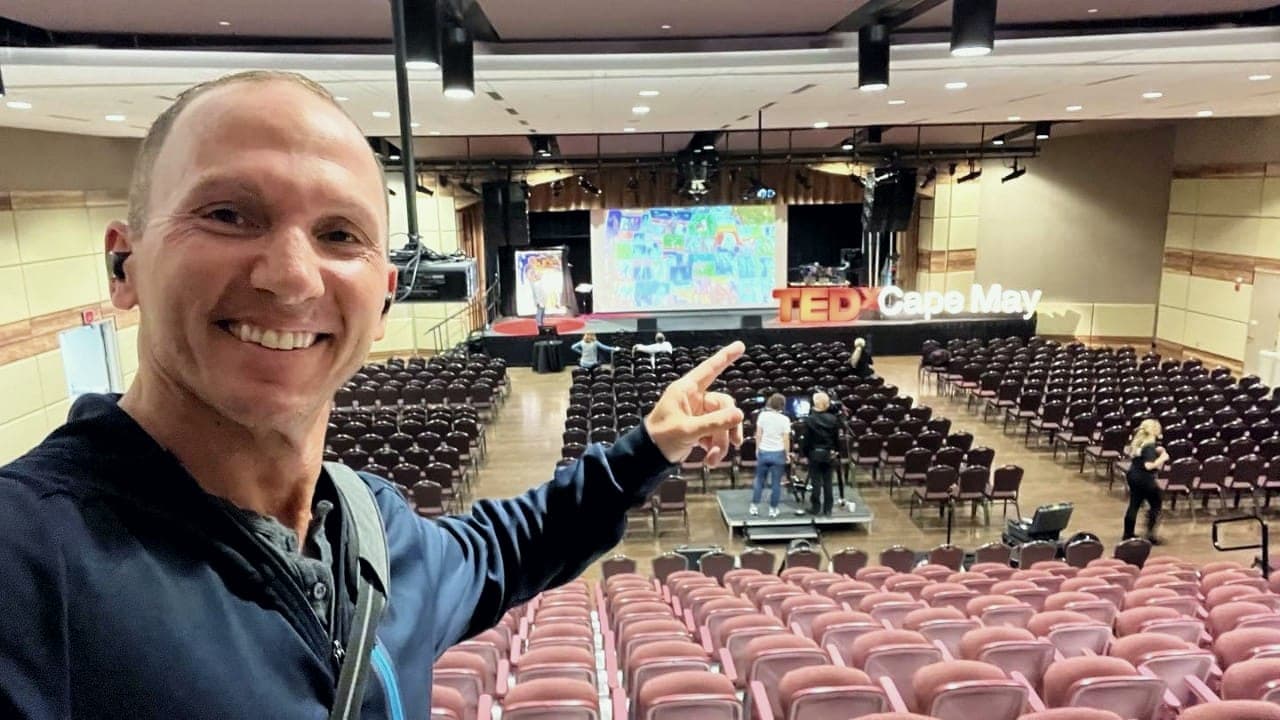 Kevin smiling and pointing to the TEDxCapeMay stage in an empty auditorium before the event